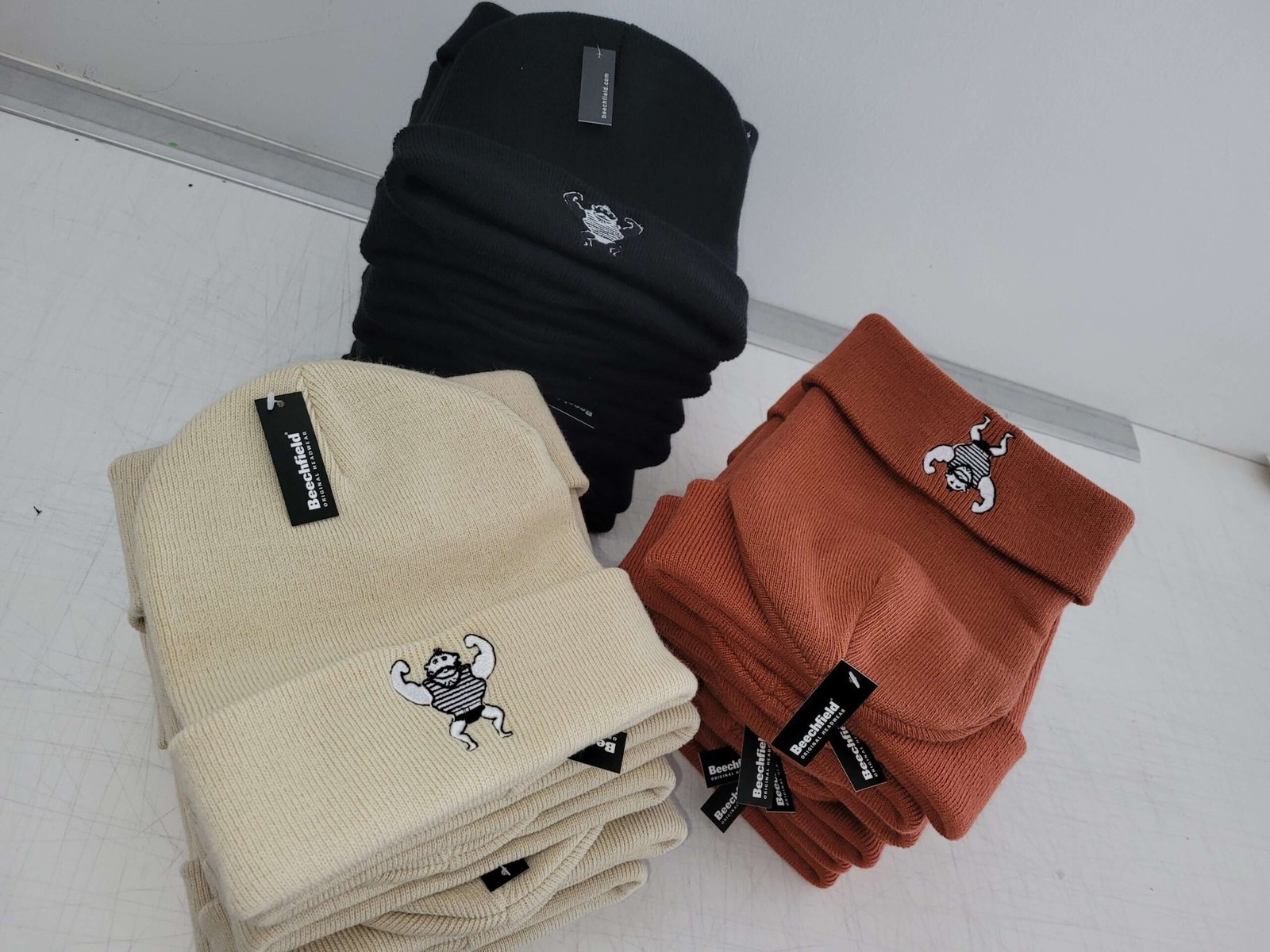 Gestapelte Beanies in Schwarz, Naturweiß und Terrakotta mit gesticktem Logo