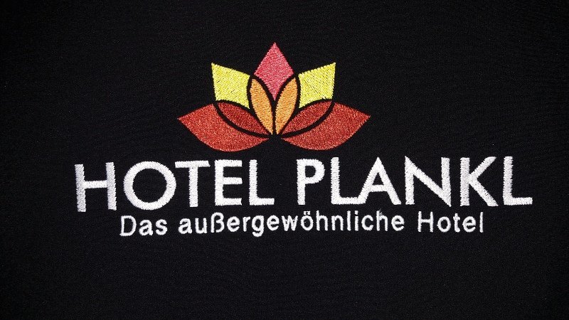 Mehrfarbig gesticktes Hotellogo mit Blütenmotiv auf dunklem Stoff